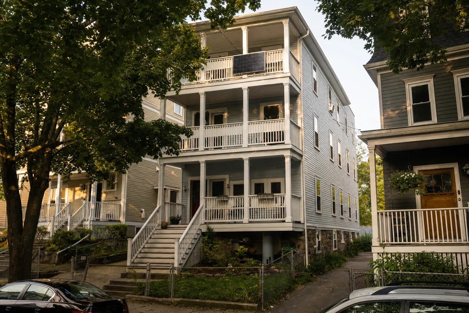 A solar panel on the top porch railing of a New England triple-decker
